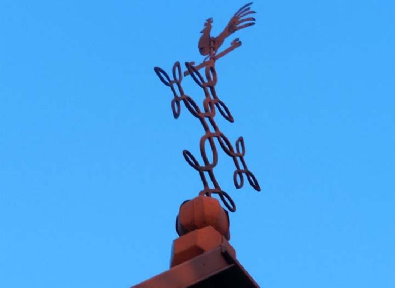 Wiatrowskaz z kogutem na krzyżu przy sanktuarium Maryjnym w Janowie na tle błękitnego nieba